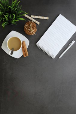 Ofis masaüstü arka planında bir fincan kahve ve yazma aletleri var. Müdürün masası, kalemi, defteri..