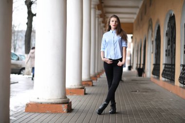 Genç, güzel bir kız, elinde kolon olan bir binanın yanında yürüyor.