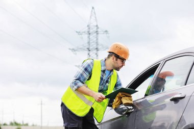 Kasklı ve üniformalı bir adam, sahada bir elektrikçi. Profesyonel elektrik mühendisi elektrik hatlarını inceliyor..