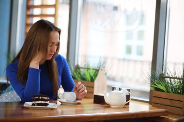 Kafede oturan ve tatlıyla çay içen genç bir kız.