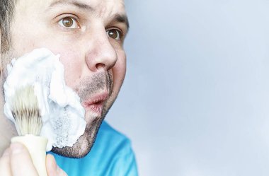 Bir adam aynanın önünde tıraş olur. Tıraş köpüğü. Tek kullanımlık jilet..