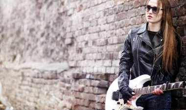 Güzel genç kız rocker elektro gitar ile. Bir gitar ile deri ceketli bir rock müzisyen kız şarkı söylüyor. Rock band solist gitar çalıyor ve mikrofona bağırır.