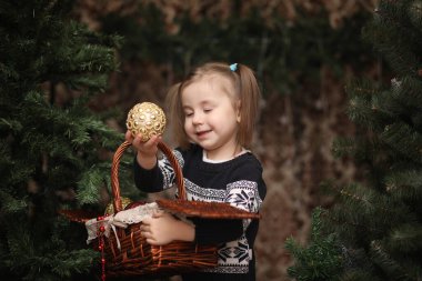 Yeni yıl ağacının yanında küçük bir çocuk. Çocuklar Noel ağacını süsler. Stüdyoda yeşil bir ağacın yanındaki süveterli bebek.