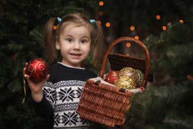 Yeni yıl ağacının yanında küçük bir çocuk. Çocuklar Noel ağacını süsler. Stüdyoda yeşil bir ağacın yanındaki süveterli bebek.