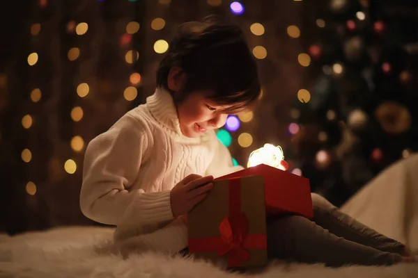 Family on Christmas eve at fireplace. Kids opening Xmas presents. Children under Christmas tree with gift boxes. Decorated living room with traditional fire place. Cozy warm winter evening home.