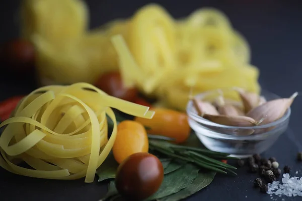 Pasta on the table with spices and vegetables. Noodles with vegetables for cooking on black stone background.