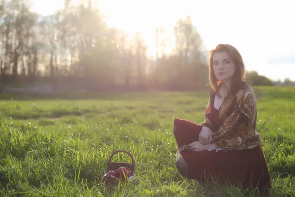 A girl in a hat on a walk in the park. A girl with a basket walks in the spring. Girl is walking along the road at sunset