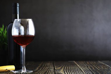 Masada bir bardak kırmızı şarap. Siyah şişe ve bir bardak şarap..