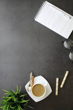 Ofis masaüstü arka planında bir fincan kahve ve yazma aletleri var. Müdürün masası, kalemi, defteri..