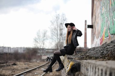 Şapkalı ve dışarıda siyah makyajlı güzel bir kız. Sokakta Gotik tarzında bir kız. Şehir caddesinde bir kız yürüyor. Deri yelekli ve telefonlu.