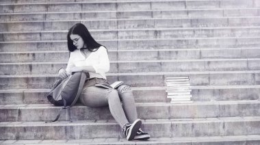 Sırt çantası ve kitapla sokaktaki genç kız.