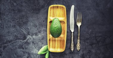 Avokado yemek tarifleri. Tahta kesme tahtasında servis edilen olgun yeşil avokado..