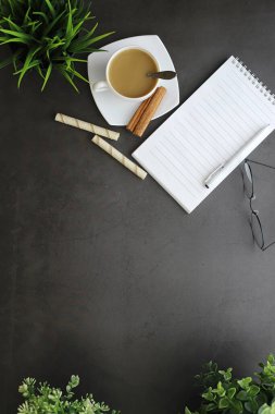 Ofis masaüstü arka planında bir fincan kahve ve yazma aletleri var. Müdürün masası, kalemi, defteri..