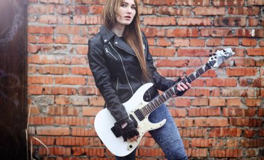 Güzel genç kız rocker elektro gitar ile. Bir gitar ile deri ceketli bir rock müzisyen kız şarkı söylüyor. Rock band solist gitar çalıyor ve mikrofona bağırır