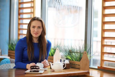 Kafede oturan ve tatlıyla çay içen genç bir kız.