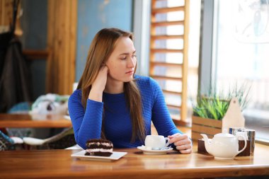Kafede oturan ve tatlıyla çay içen genç bir kız.