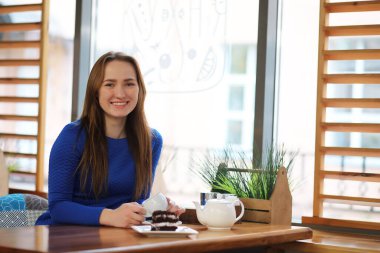 Kafede oturan ve tatlıyla çay içen genç bir kız.
