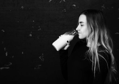 Genç kız siyah duvardaki bir şişeden süt içiyor.