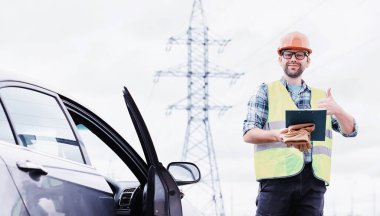 Kasklı ve üniformalı bir adam, sahada bir elektrikçi. Profesyonel elektrik mühendisi elektrik hatlarını inceliyor..