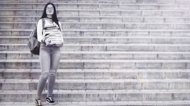 Sırt çantası ve kitapla sokaktaki genç kız.