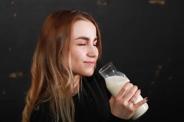 若い女の子は黒壁の背景にボトルからミルクを飲む — ストック写真