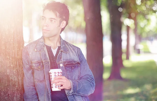 A young man walks in the park at lunch time. A man is on a walk in the city. A student in park