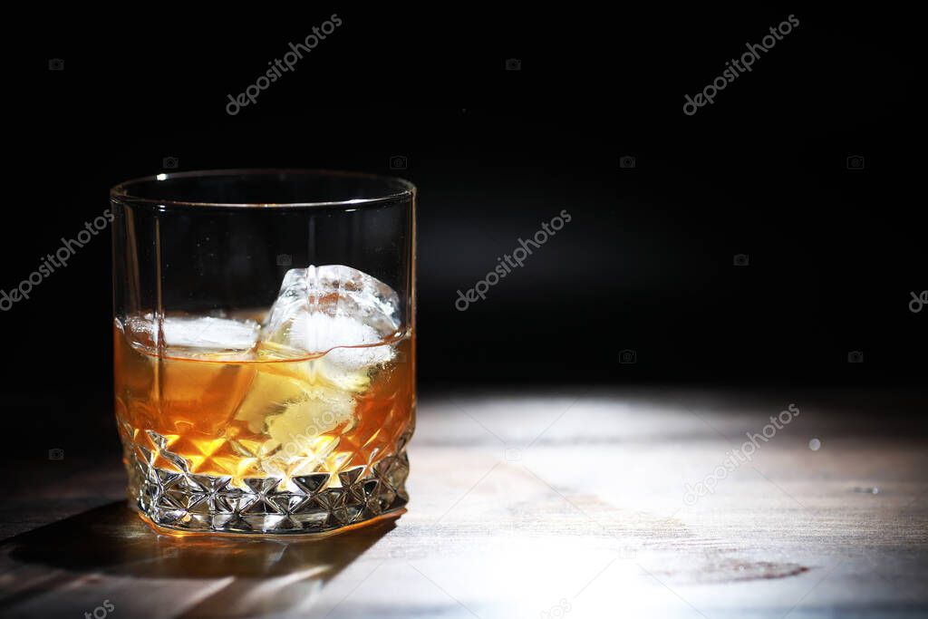 A glass of strong alcoholic drink with ice on wooden bar counter. Whiskey with ice cubes. Glass with a chilled drink.
