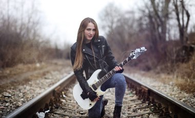 Güzel genç kız rocker elektro gitar ile. Bir gitar ile deri ceketli bir rock müzisyen kız şarkı söylüyor. Rock band solist gitar çalıyor ve mikrofona bağırır