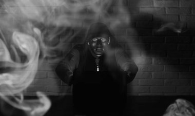 Siyah maskeli ve başlıklı bilgisayar korsanı Monito 'nun önündeki masada.