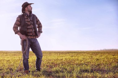Şapkalı bir kovboy ve güneş altında bir tarlada duran bir kementle.