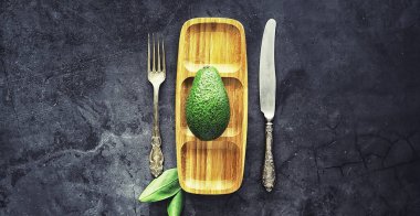 Avokado yemek tarifleri. Tahta kesme tahtasında servis edilen olgun yeşil avokado..