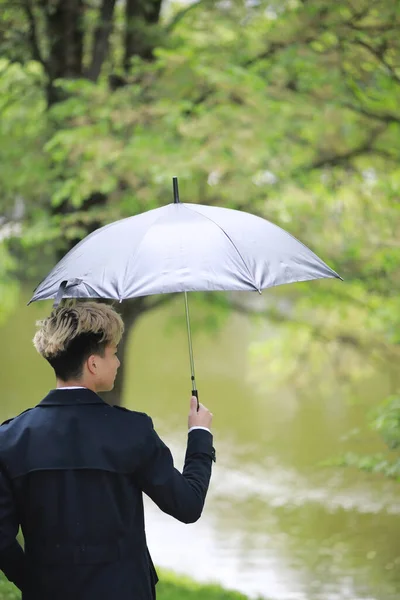 雨の日の春の公園と傘を持った若い男 — ストック写真