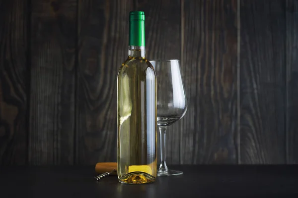 Transparent bottle of white dry wine on the table. White wine glass on a wooden wall background.