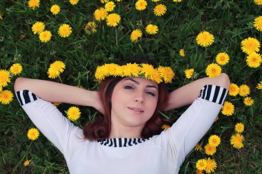 Güneşli bir günde, sarı bir karahindiba çayırında dinlenen bir kız.