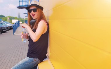 Güneş gözlüklü ve şapkalı genç kız. Duvardaki hippi kız. Sokakta şapkalı ve gözlüklü bir genç