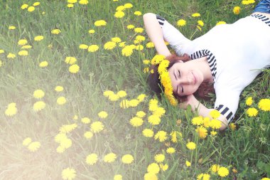 Güneşli bir günde, sarı bir karahindiba çayırında dinlenen bir kız.
