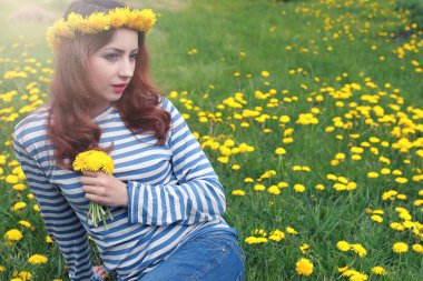 Güneşli bir günde, sarı bir karahindiba çayırında dinlenen bir kız.