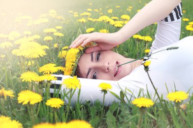 Güneşli bir günde, sarı bir karahindiba çayırında dinlenen bir kız.