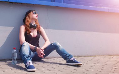 Güneş gözlüklü ve şapkalı genç kız. Duvardaki hippi kız. Sokakta şapkalı ve gözlüklü bir genç