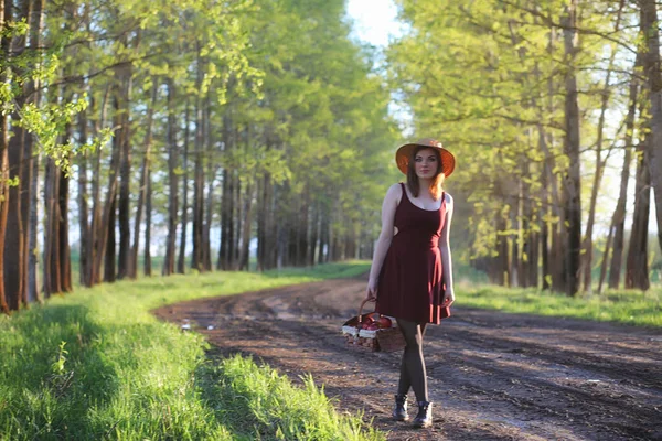 stock image A girl in a hat on a walk in the park. A girl with a basket walks in the spring. Girl is walking along the road at sunset