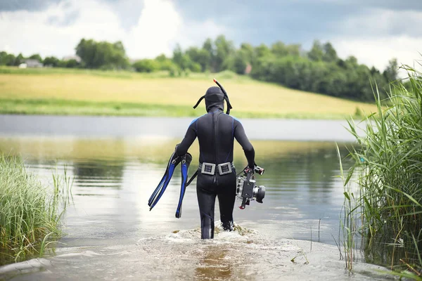 A scuba diver in a wet suit prepares to immerse in a pond