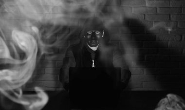 Siyah maskeli ve başlıklı bilgisayar korsanı Monito 'nun önündeki masada.