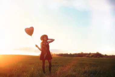 Parkta yürüyüş yapan şapkalı bir kız. Sepetli bir kız sonbaharda yürür. Kız gün batımında yolda yürüyor.