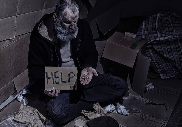 A homeless bearded man sits on boxes on street and asks for help. Need a homeless person asks for money for food and overnight.
