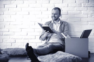 Sakallı bir adam elinde kağıtla yerde oturuyor.