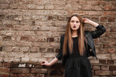 Şapkalı ve dışarıda siyah makyajlı güzel bir kız. Sokakta Gotik tarzında bir kız. Şehir caddesinde bir kız yürüyor. Deri yelekli ve telefonlu.