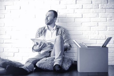 Sakallı bir adam elinde kağıtla yerde oturuyor.