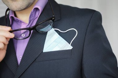 Tek kullanımlık bir tıbbi maske peçeteden sarkıyor. Takım elbiseli ve kot pantolonlu tek kullanımlık maskeli bir adam. Bireysel solunum koruması.