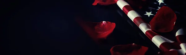 American flag and rose flower on table. Symbol of the United States of America and red petals. Patriotism and memory.