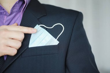 Tek kullanımlık bir tıbbi maske peçeteden sarkıyor. Takım elbiseli ve kot pantolonlu tek kullanımlık maskeli bir adam. Bireysel solunum koruması.